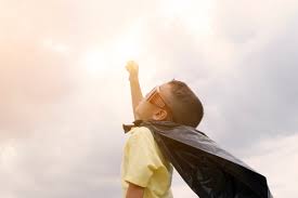 alt="young boy with cape pointing fist to the sky"