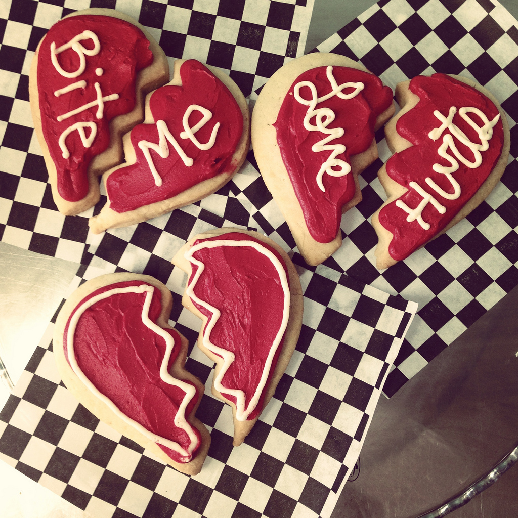 alt="three red broken heart-shaped cookies saying bite me & love hurts"
