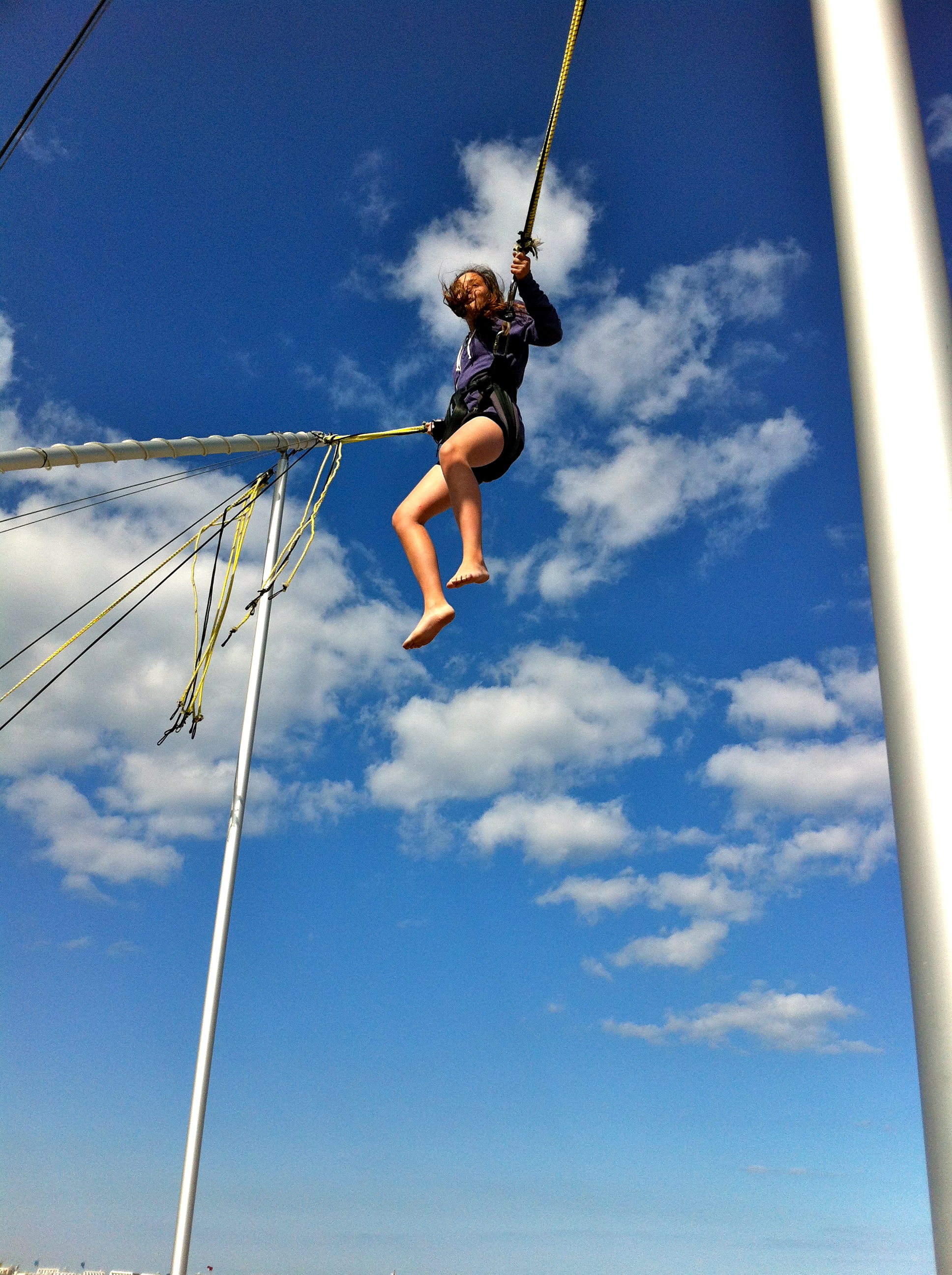 alt="girl in harness jumping up into the blue sky"