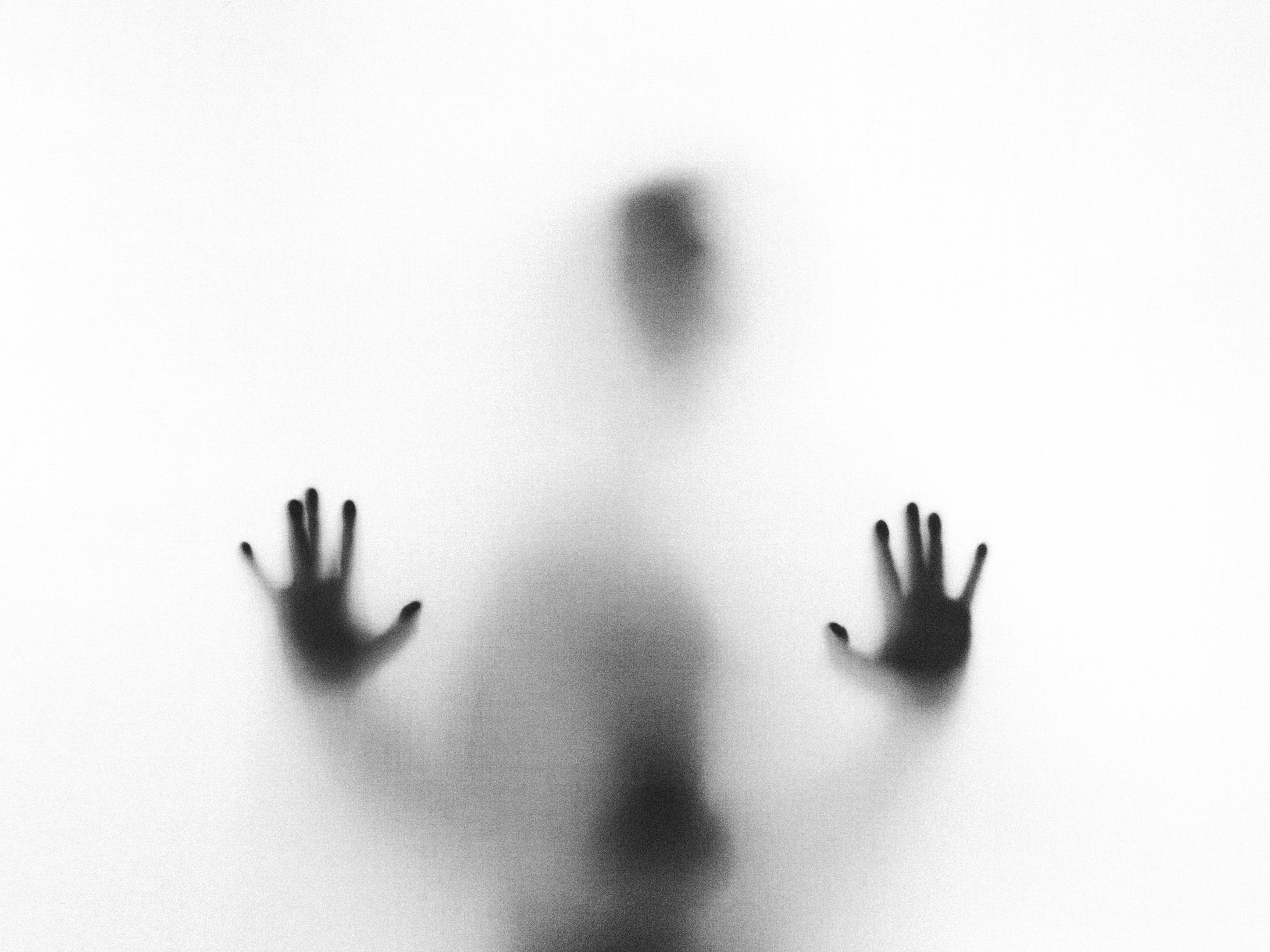 alt="shady figure with hands against frosted glass"